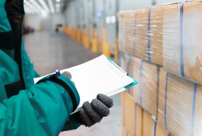 Warehouse staff checking inventory records beside stacked cartons